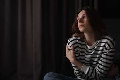 Photo of Sad young woman near curtains indoors, space for text