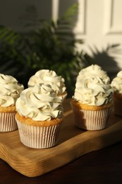 Photo of Tasty cupcakes with vanilla cream on wooden table, closeup