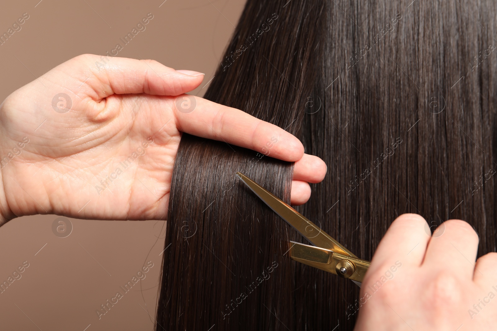 Photo of Hairdresser cutting client's hair with scissors on light brown background, closeup