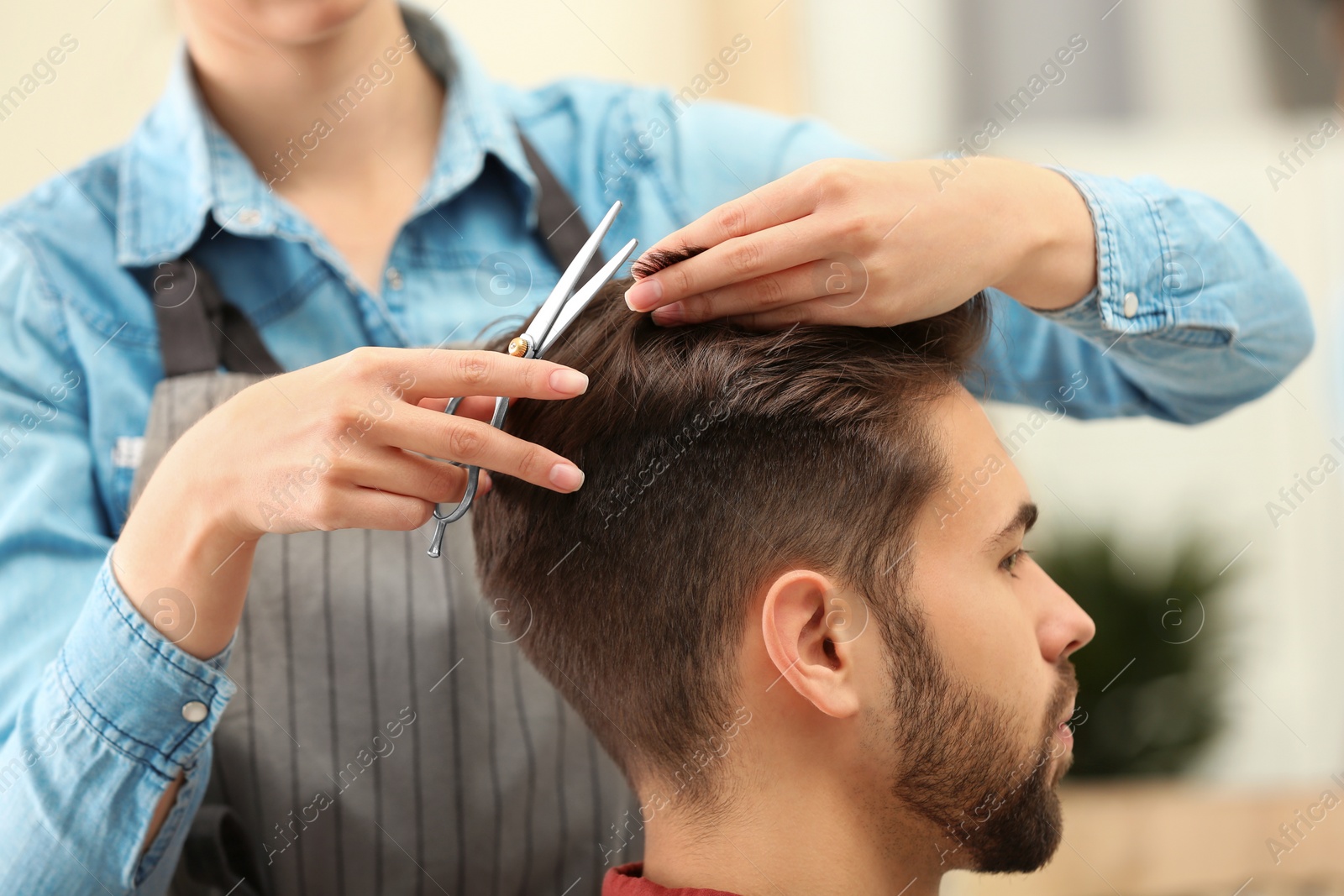 Photo of Barber making stylish haircut with professional scissors in beauty salon