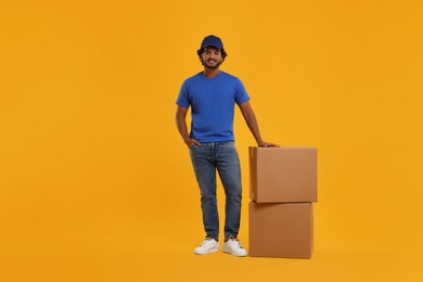 Happy young courier with parcels on orange background