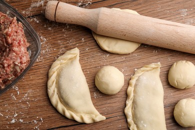 Photo of Dough, minced meat and rolling pin on wooden table, flat lay. Making chebureki