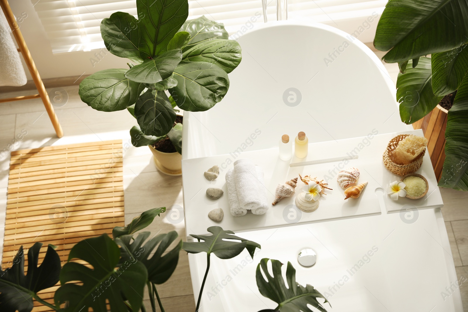 Photo of Bath tray with spa products, towels and shells on tub in bathroom, above view. Interior design