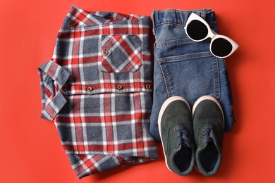 Photo of Stylish child clothes, shoes and sunglasses on red background, flat lay