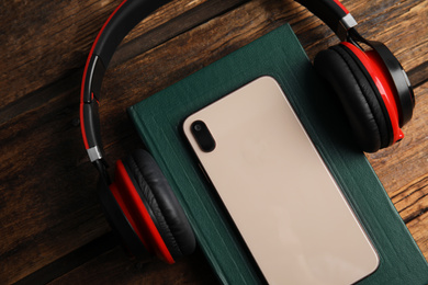 Book, modern headphones and smartphone on wooden table, closeup