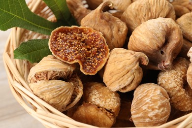 Photo of Wicker basket with tasty dried figs and green leaf on table, closeup