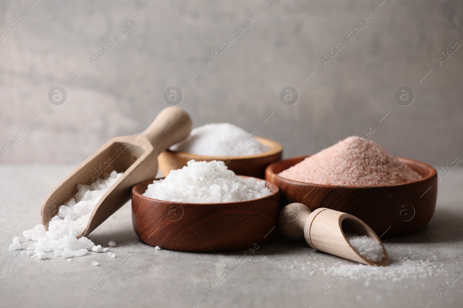 Photo of Different natural salt in scoops and bowls on grey table