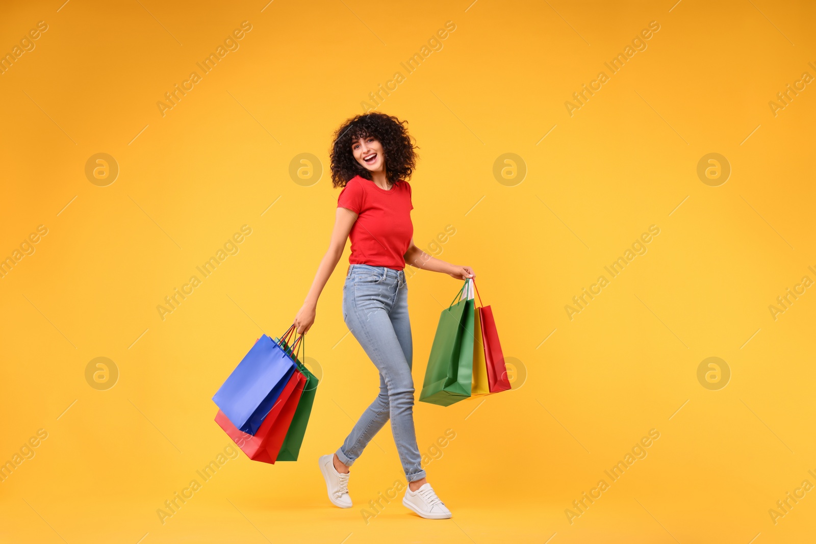 Photo of Happy young woman with shopping bags on yellow background