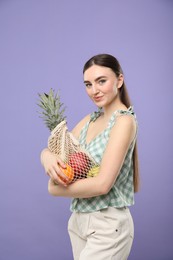 Photo of Woman with string bag of fresh fruits on violet background