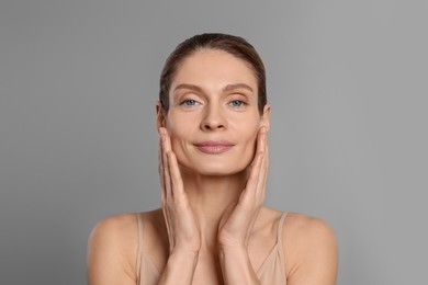 Woman massaging her face on grey background