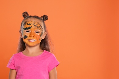 Photo of Cute little girl with face painting on orange background. Space for text
