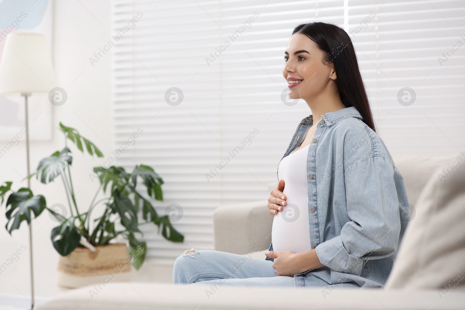 Photo of Happy pregnant woman on sofa at home, space for text