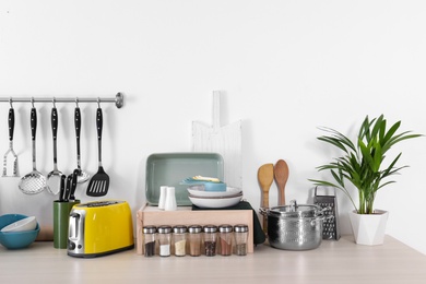Photo of Set of clean cookware, dishes, utensils and appliance on table at white wall