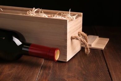Photo of Open wooden crate with bottle of wine on table