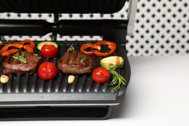 Photo of Electric grill with tasty meat, spices and vegetables on white table, space for text