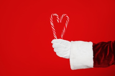 Photo of Santa Claus holding candy canes on red background, closeup of hand