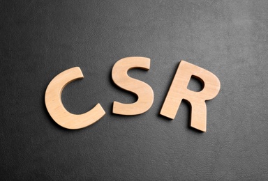 Photo of Wooden letters CSR on black background, flat lay. Corporate social responsibility concept