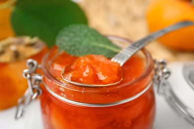 Jar and spoon of tasty persimmon jam, closeup view