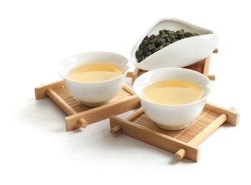 Photo of Cups of Tie Guan Yin oolong and chahe with tea leaves on white background