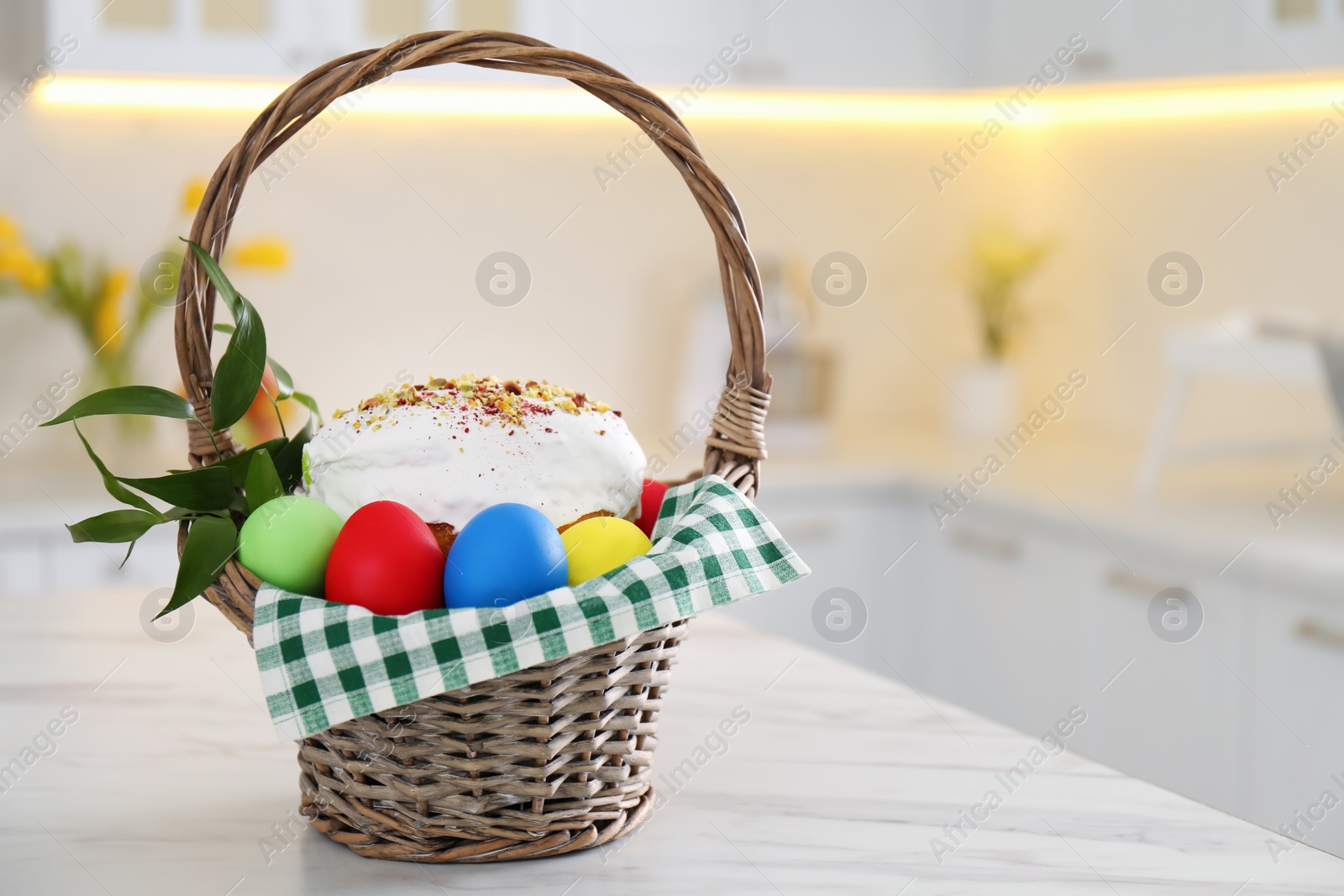 Photo of Basket with delicious Easter cake and dyed eggs on white table in kitchen. Space for text