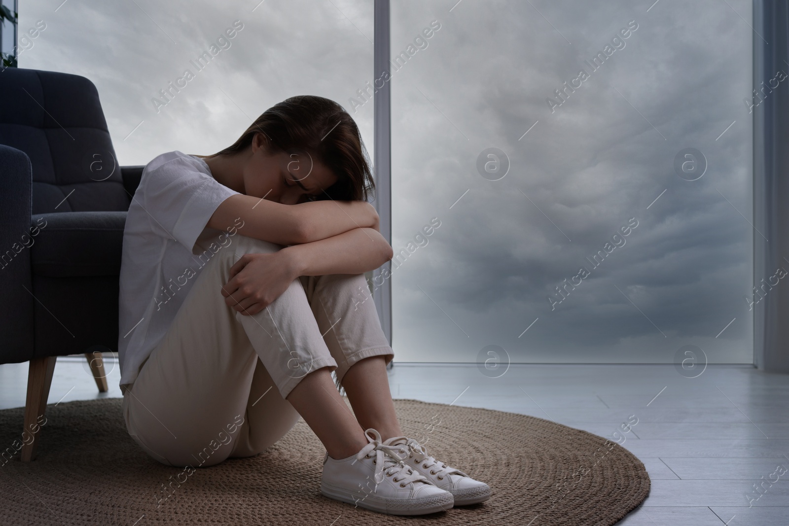 Photo of Sad young woman sitting on floor at home, space for text. Loneliness concept