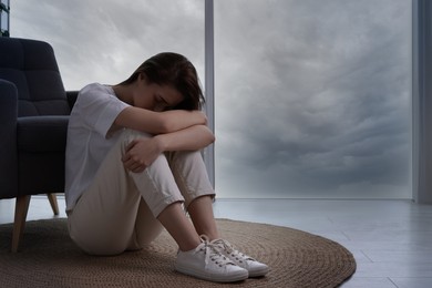 Photo of Sad young woman sitting on floor at home, space for text. Loneliness concept