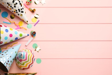 Flat lay composition with party hats, blowers and confetti on light pink wooden background. Space for text