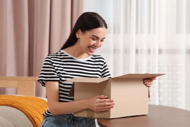 Emotional young woman opening parcel at home. Internet shopping