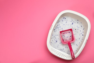 Photo of Cat litter tray with filler and scoop on pink background, top view. Space for text