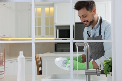 Photo of Man washing plate above sink in kitchen, view from outside