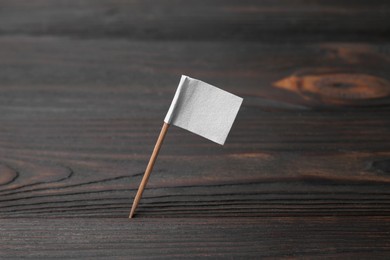 Photo of Small white paper flag on wooden table, closeup