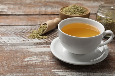 Photo of Aromatic fennel tea in cup and seeds on wooden table, closeup. Space for text