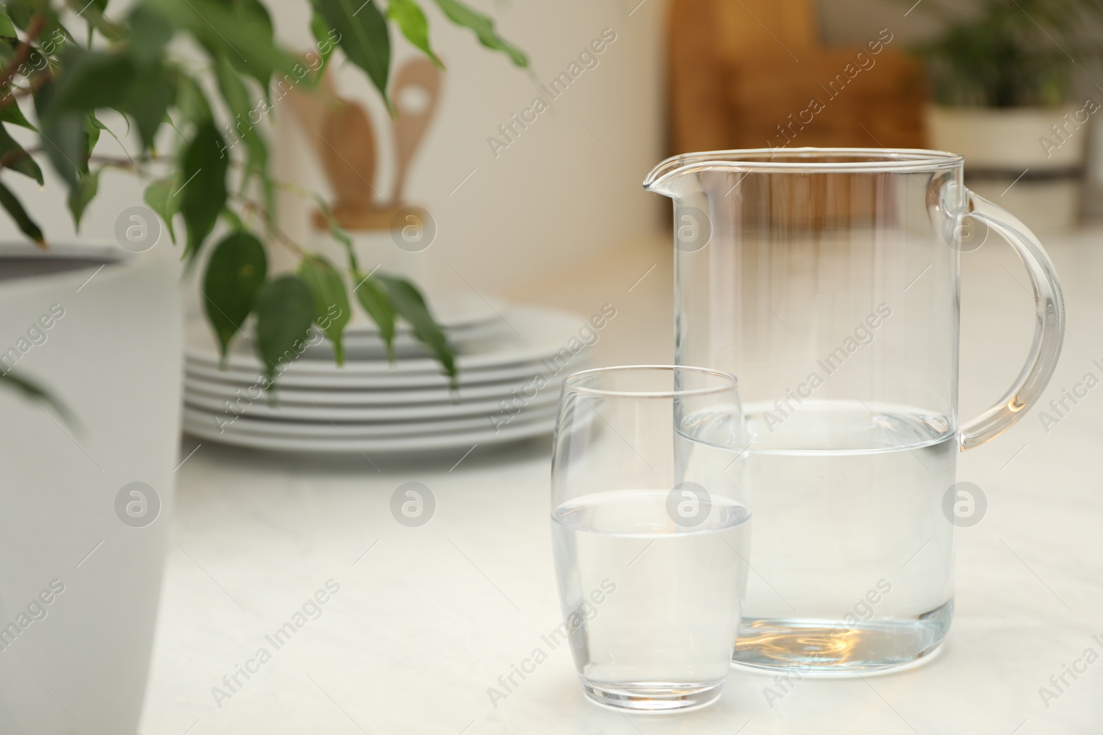 Photo of Jug and glass with clear water on white table in kitchen, space for text