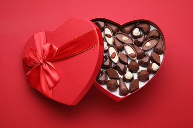 Photo of Heart shaped box with delicious chocolate candies on red background, top view