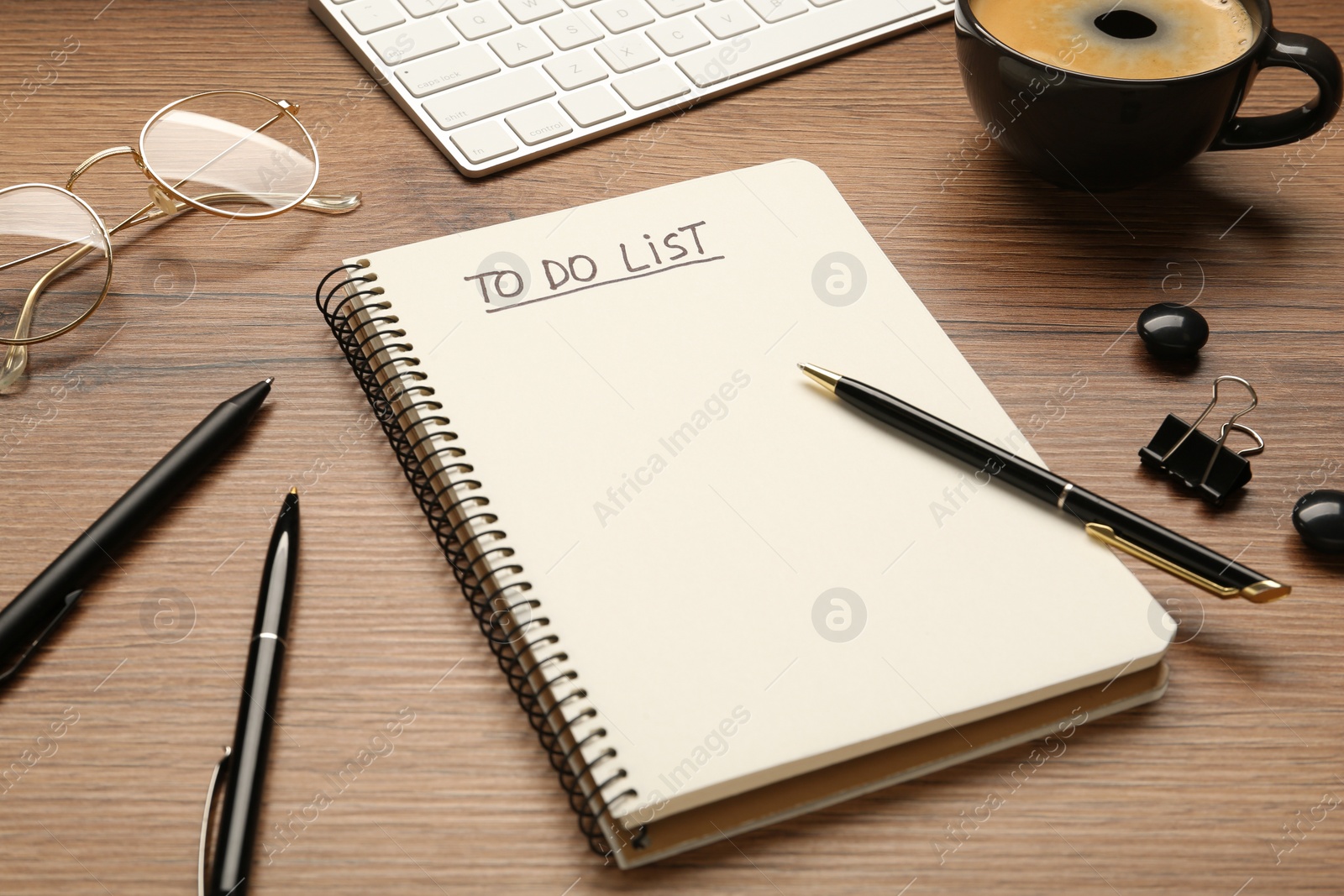 Photo of Notepad with inscription To Do List, pens, glasses and cup of coffee on wooden table