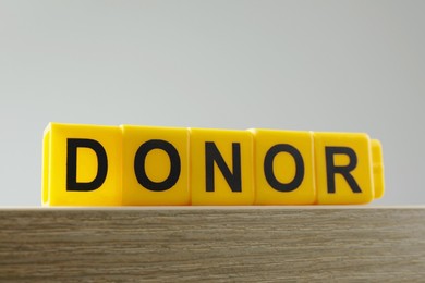 Word Donor made of yellow cubes on wooden table, closeup