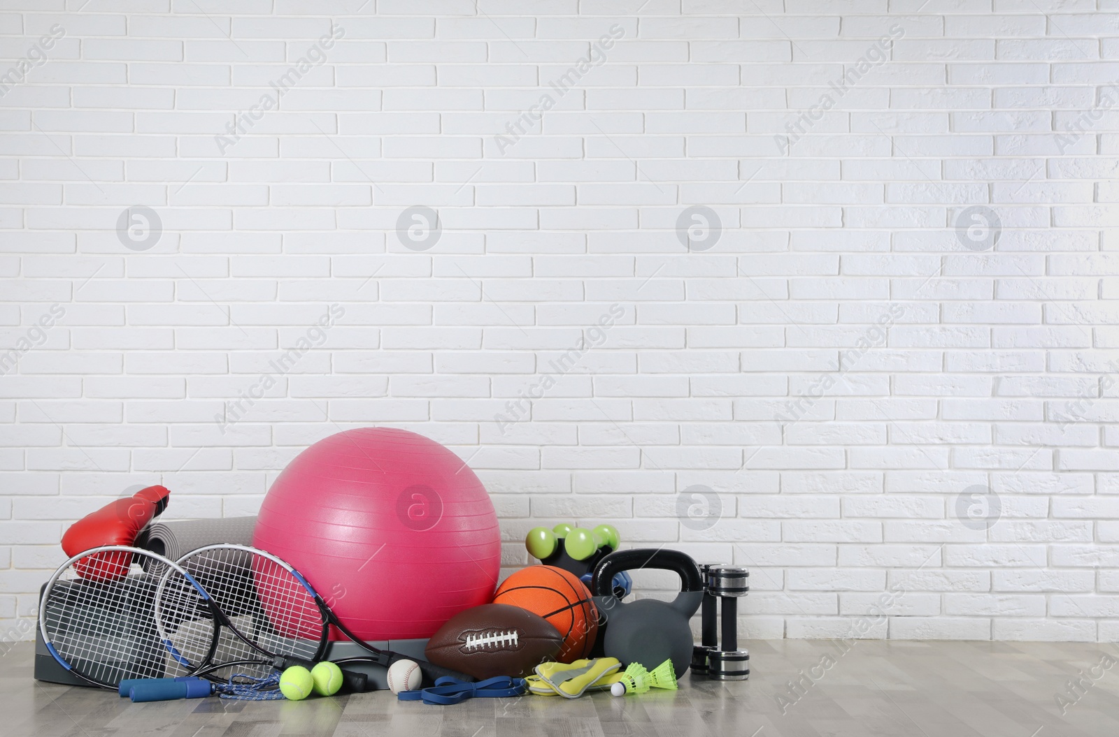 Photo of Set of different sports equipment on floor near white brick wall, space for text