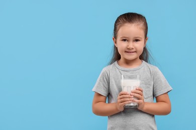 Photo of Cute girl with glass of fresh milk on light blue background, space for text