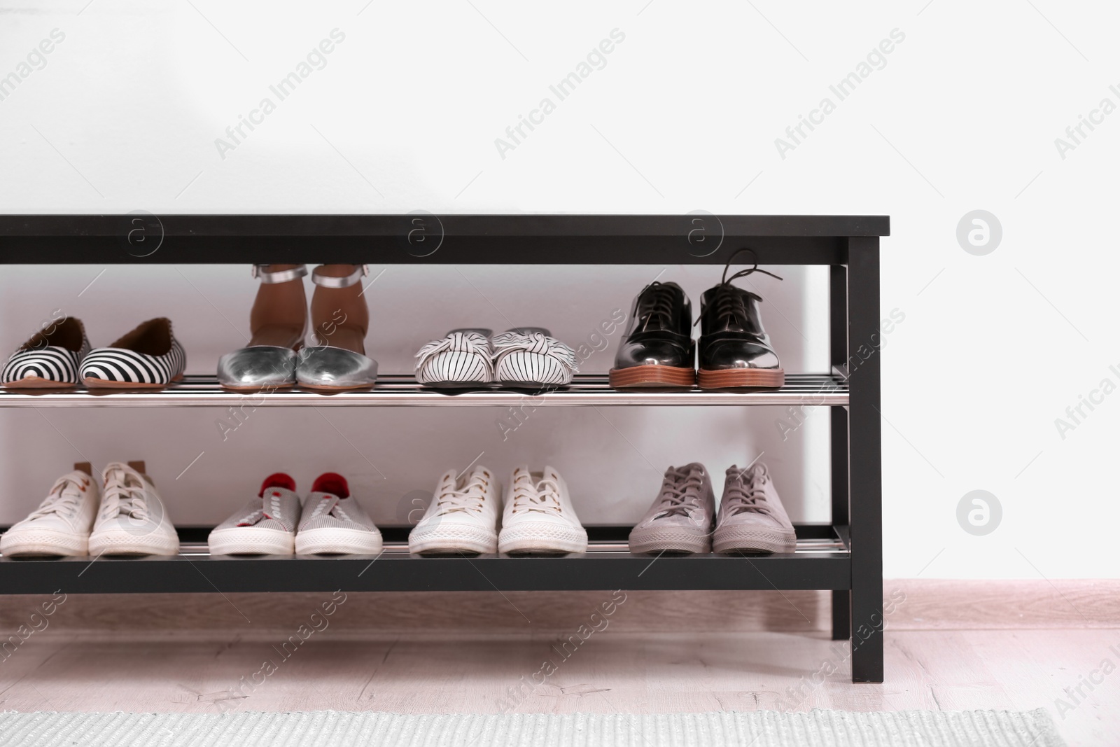 Photo of Shoe rack with different footwear near white wall. Stylish hallway interior