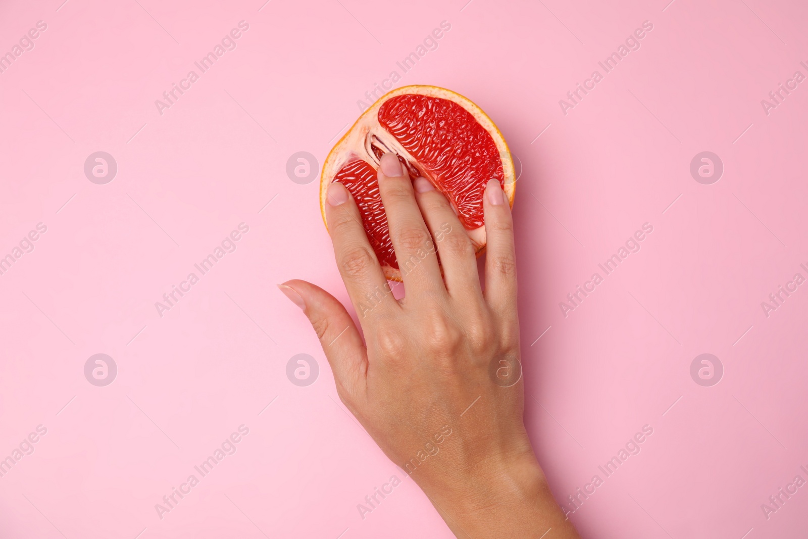 Photo of Young woman touching half of grapefruit on pink background, top view. Sex concept