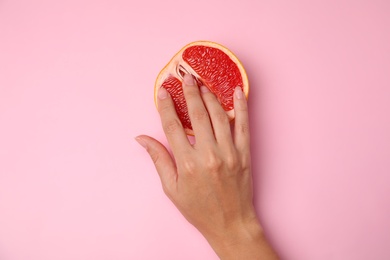 Photo of Young woman touching half of grapefruit on pink background, top view. Sex concept