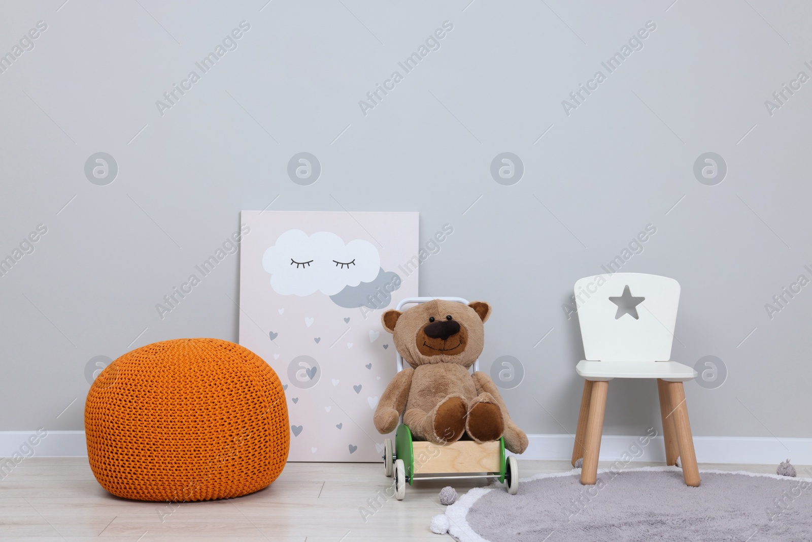 Photo of Kindergarten interior. Small chair, toy, ottoman and picture near grey wall