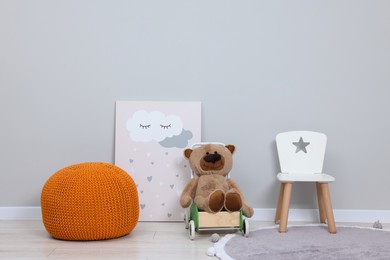 Kindergarten interior. Small chair, toy, ottoman and picture near grey wall