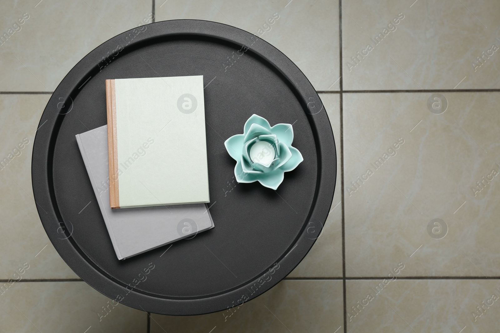 Photo of Candle in beautiful flower shaped holder and books on black table, top view