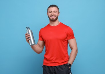 Handsome man with thermo bottle on light blue background, space for text