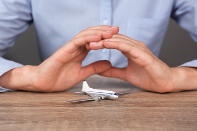 Insurance agent covering toy plane at table, closeup. Travel safety concept