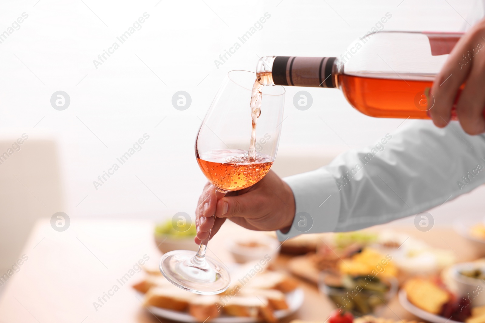 Photo of Man pouring rose wine from bottle into glass indoors, closeup. Space for text