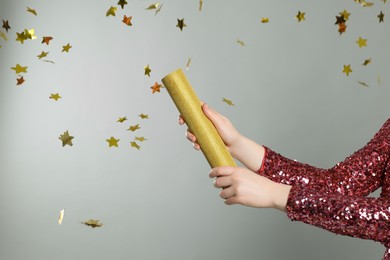 Photo of Young woman blowing up party popper on light grey background, closeup