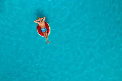 Happy man with inflatable ring in swimming pool, top view and space for text. Summer vacation