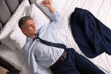 Businessman in office clothes sleeping on bed indoors, top view